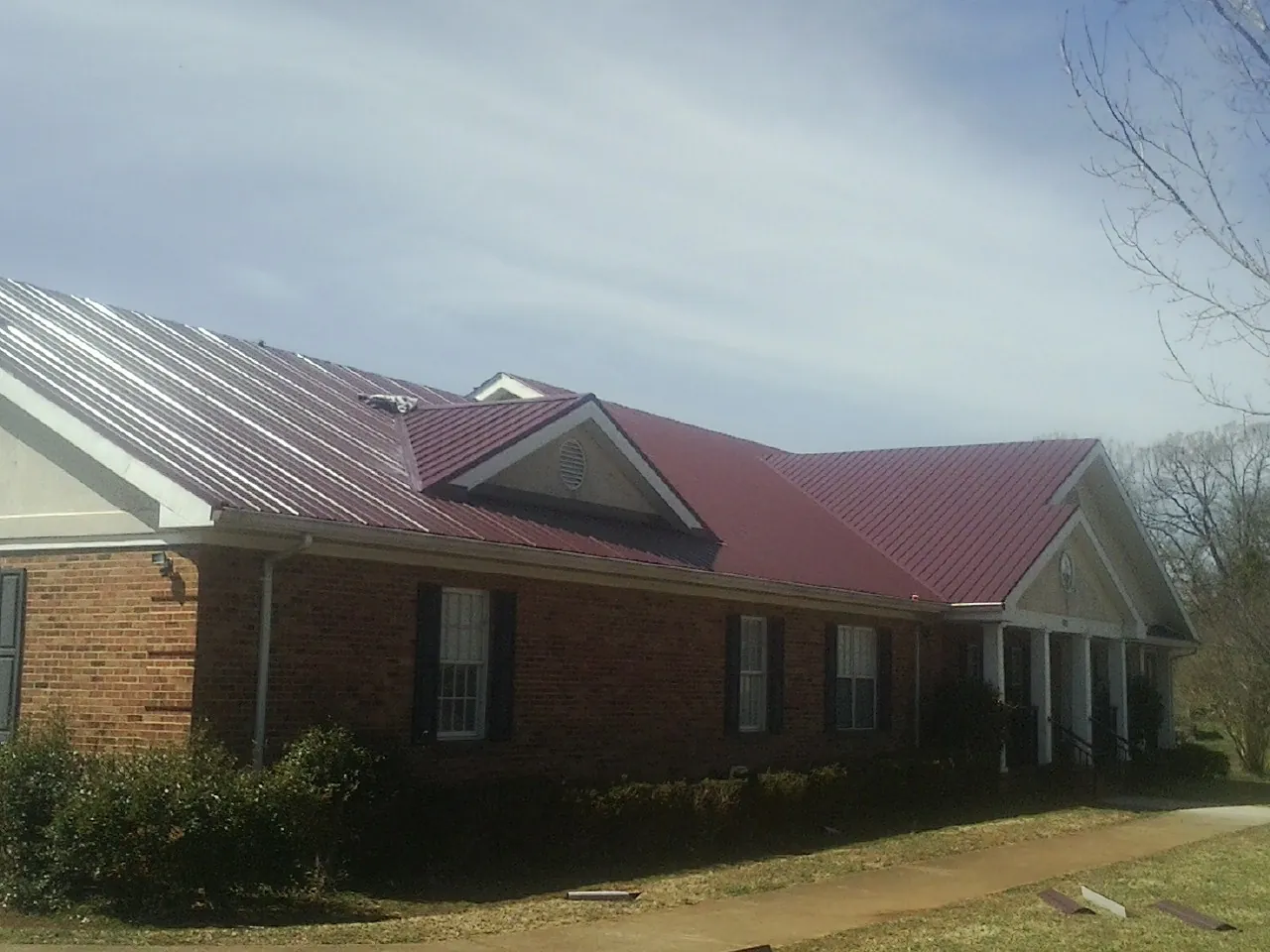 Red metal roof with gabled entries on a long brick building, from a Hail Damage Roof Repair job in Tea