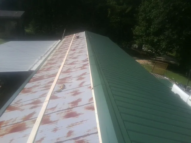 Old rusted panels beside newly installed green metal roofing — Wind Damage Roof Repair by Roofing Brothers in Tea