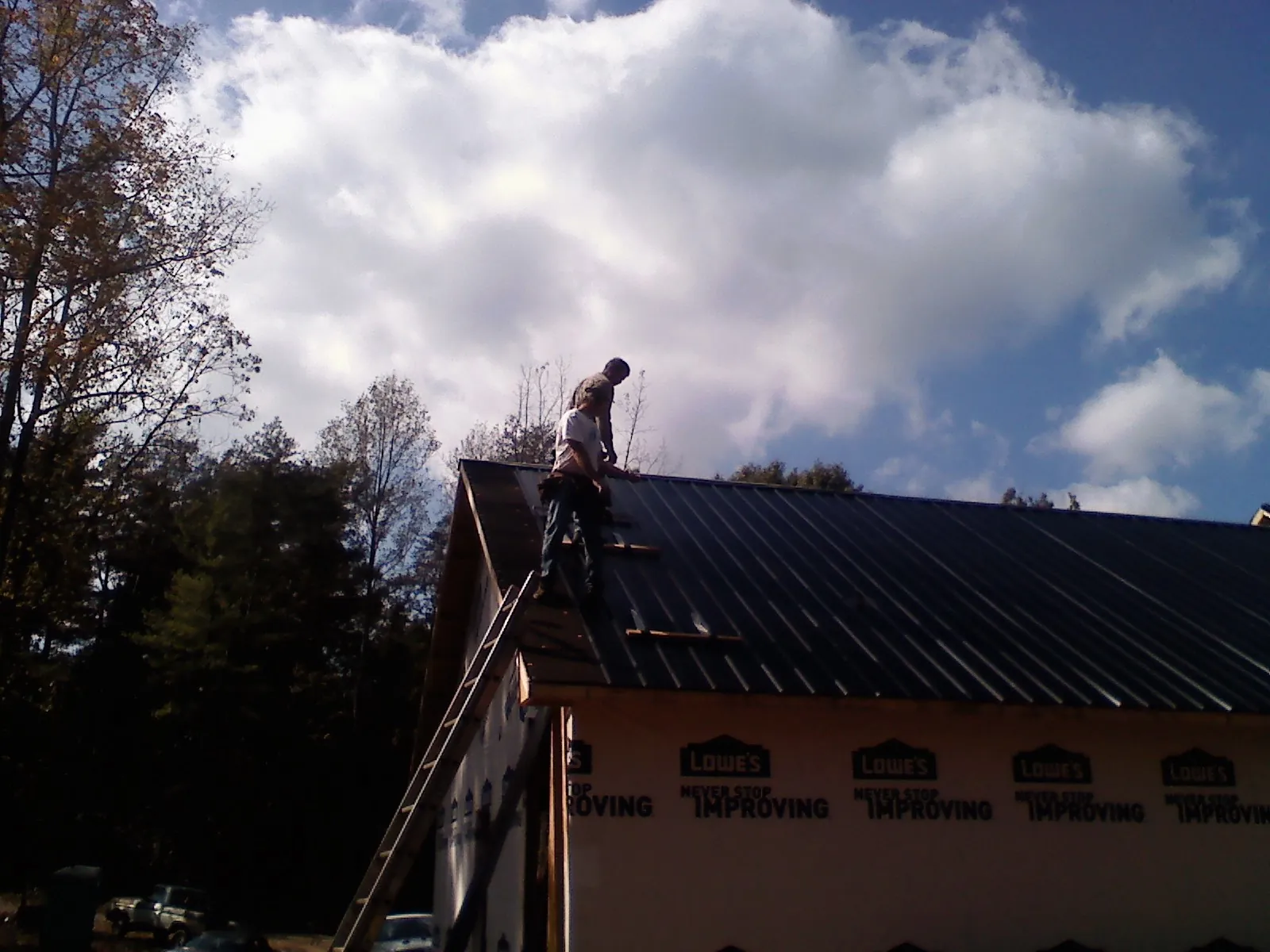 Roofer fastening dark metal panels high against a cloudy sky, from a Roof Inspection job in Tea